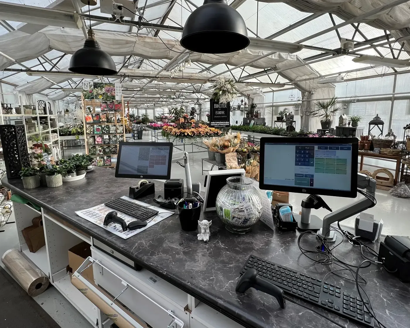 Kassanova Garden i drift i en trädgårdsbutik med kassaskärmar, streckkodsläsare och kvittoskrivare